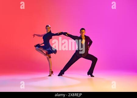 Junger Mann und Frau, Tänzerinnen im Ballsaal tanzen ausdrucksvoll energiegeladene Zumba in Neonlicht vor lebendigem Hintergrund mit Farbverlauf. Stockfoto