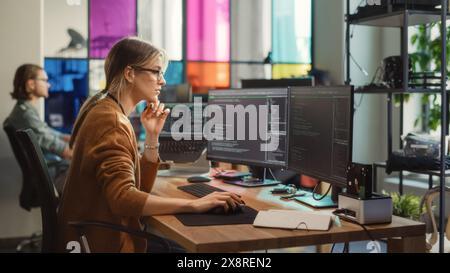 Die weiße Frau schreibt Codezeilen auf einem Desktop-PC mit mehreren Displays und einem Laptop im eleganten Büro. Professionelle Datenwissenschaftlerin mit Software zur Analyse von Informationen aus dem Internet. Stockfoto