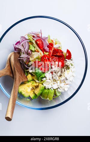 Feta- und Avocadosalat mit Tomaten und roten Zwiebeln in einer Glasschale, weißer Hintergrund. Stockfoto