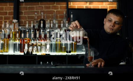 Nahaufnahme eines Barkepers an einer Bar, der Alkohol in ein Vintage-Glas gießt. Medien. Gießen Sie rote heiße alkoholische Tinktur mit Dampf. Stockfoto