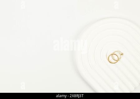 Blick von oben auf goldene Hochzeitsringe auf weißem Hintergrund. Abstrakte Hochzeitskomposition, weißes Bogentablett, Podium. Kopierraum, flach. Stockfoto