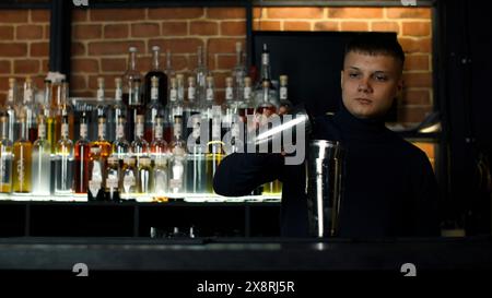 Junger männlicher Barkeeper, der Shaker für die Zubereitung des Alkoholgetränks benutzt. Aktion. Partykonzept im Nachtclub. Stockfoto