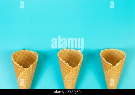 Blick von oben auf drei Eiswaffelkegel auf blauem Hintergrund. Sommertapete, flach, Kopierraum. Stockfoto
