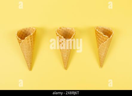 Blick von oben auf drei Eiswaffelkegel auf gelbem Hintergrund. Sommertapete, flach, Kopierraum. Stockfoto