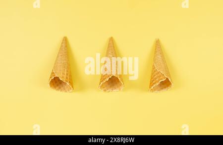 Blick von oben auf drei Eiswaffelkegel auf gelbem Hintergrund. Sommertapete, flach, Kopierraum. Stockfoto