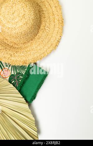 Blick von oben auf Strohhut, getrocknete Palmblätter und grüne Handtücher auf weißem Hintergrund. Sommermode, Urlaubs- und Strandtapete. Kopierraum, flach. Stockfoto