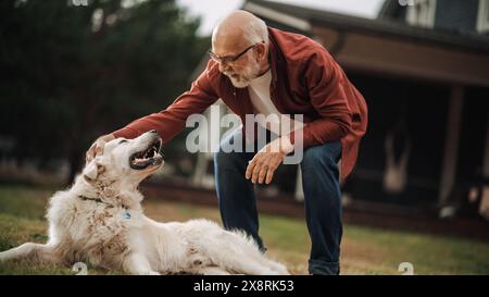 Glücklicher Erwachsener, der die Zeit im Freien mit einem weißen Goldenen Retriever genießt und einen verspielten energetischen Haustierhund streichelt. Fröhlicher Seniorenmann, der Zeit mit einem Haustier auf einem Rasen vor dem Haus verbringt. Stockfoto