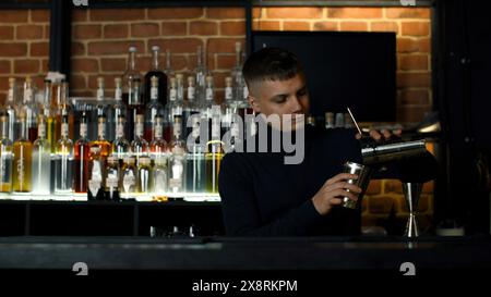 Junger männlicher Barkeeper, der Shaker für die Zubereitung des Alkoholgetränks benutzt. Aktion. Partykonzept im Nachtclub. Stockfoto