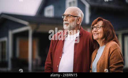Fröhliches altes Paar, das sich im Haus der Vororte im Freien aufhält und sich umschließt. Erwachsene in lebenslanger Beziehung Blick auf die Kamera und Lächeln, genießen ihr gesundes Seniorenleben. Stockfoto