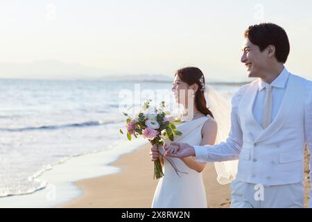 Japanisches frisch verheiratetes Paar, das am Strand spaziert Stockfoto