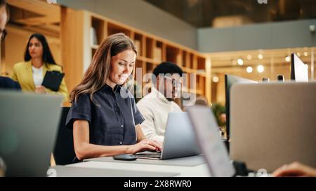 Multiethnische kreative Kollegen, die tagsüber in einem geschäftigen Büro mit Laptops arbeiten. Personalabteilung, die an der Planung arbeitet. Weibliche Mitarbeiterin Lächelt Stockfoto