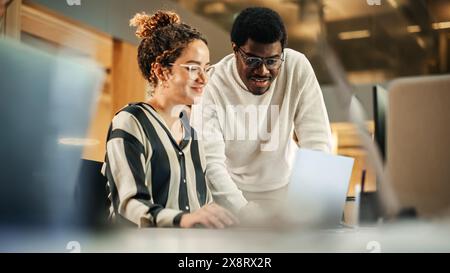 Porträt zweier kreativer Kollegen, die Laptop verwenden, um das Arbeitsprojekt im Büro zu diskutieren. Young Black Technical Support Specialist Hilft Weiblicher Customer Relationship Coordinator. Teamwork-Konzept Stockfoto