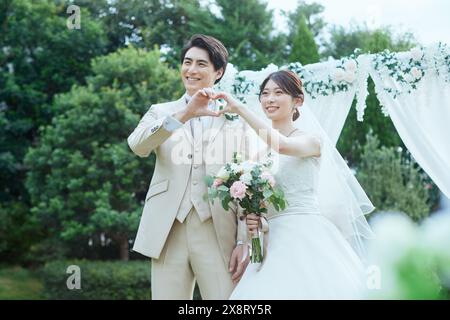 Japanische Braut und Bräutigam stehen vor einem Hochzeitsbogen Stockfoto