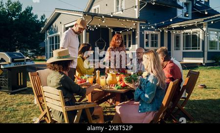 Große Familie und Freunde feiern draußen zu Hause. Verschiedene Gruppen von Kindern, Erwachsenen und alten Menschen versammelten sich an einem Tisch, um lustige Gespräche zu führen. Barbecue vorbereiten und Gemüse essen. Stockfoto