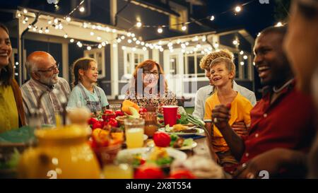 Großelternin teilt interessante Kindheitserinnerungen an ihre verschiedenen Verwandten und multiethnischen Freunde während eines Dinner Table im Freien mit geräuchertem Grillfleisch und viel frischem Gemüse. Stockfoto