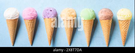 Verschiedene Eiskugeln in Kegeln auf blauem Hintergrund, Banner. Set aus veganem, bunten Bio-Eis in Waffelkegeln. Flache Lagen. Stockfoto