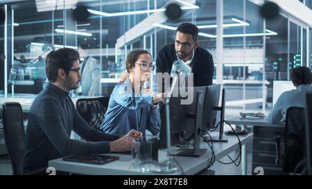 Ein Team innovativer Industrieingenieure bespricht mithilfe des Computers ein technologisches Projekt im modernen Fabrikbüro Industrie 4,0. Gruppe von Wissenschaftlern arbeitet im Forschungs- und Entwicklungszentrum. Stockfoto