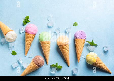 Verschiedene Eiskugeln in Kegeln auf blauem Hintergrund, Draufsicht. Komposition aus verschiedenen veganen bunten Eissorten in Waffelkegeln. Flache Lagen. Stockfoto