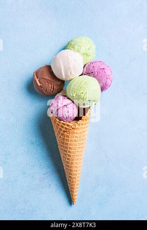 Eiskegel mit verschiedenen Schaufeln auf blauem Hintergrund, kreative flache Lay. Viele bunten Bio-Eiskugeln in Waffelkegel. Stockfoto