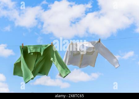 Hemden auf einer Wäscheleine trocknen in der Sonne, die sich in der Luft bewegt, mit einem blauen Himmel mit Wolken im Hintergrund Stockfoto