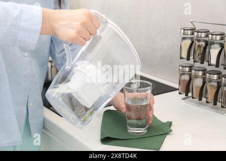 Frau, die Wasser aus dem Filterkrug in das Glas in der Küche gießt, Nahaufnahme Stockfoto