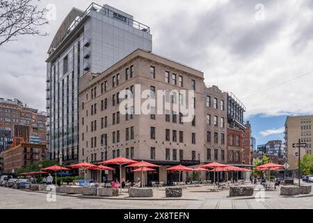 New York, NY - USA - 19. Mai 2024 Ein kopfsteingepflasterter platz mit roten Sonnenschirmen, Tischen und Stühlen im Meatpacking District, einem angesagten Geschäftsviertel auf dem f Stockfoto