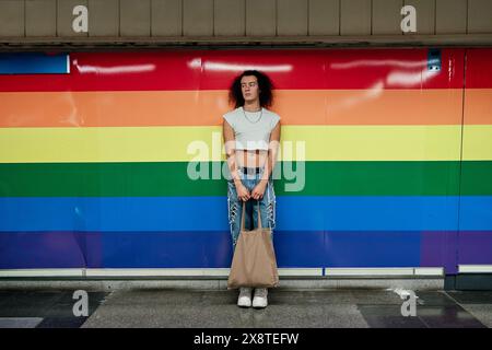 Foto eines schwulen Mannes mit lockigem Haar, das auf einem Paar in den Farben der Homosexuellen-Stolz-Flagge gezeichnet ist. Ein Mann trägt Jeans und ein verkürztes Oberteil Stockfoto