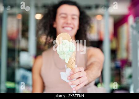 Detail eines Eiskegels, der von der Hand eines Mannes gehalten wird. Nicht fokussierter Mann im Hintergrund Stockfoto