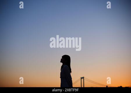 Japanische Frau, die bei Sonnenuntergang vor einer Brücke steht Stockfoto