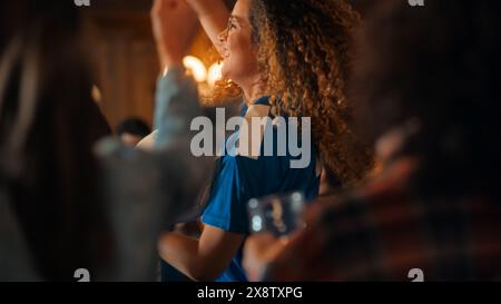 Porträt einer multiethnischen jungen Frau in einem blauen Jersey-Shirt, die in einer Menge von Sportfans in einem Pub beim Fernsehen anfeuert. Freunde, die feiern, wenn das Team ein Tor erzielt und das Turnier gewinnt. Stockfoto