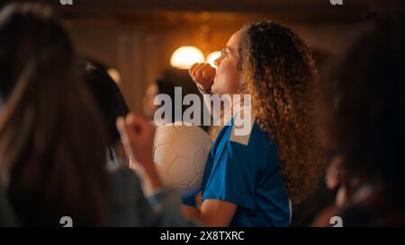 Porträt einer aufgeregten jungen Frau in einem blauen T-Shirt, die in einer Menge von Sportfans in einer Bar steht und Fernsehsendungen ansieht. Fans feiern, wenn das Team ein Tor erzielt und die Meisterschaft gewinnt. Stockfoto