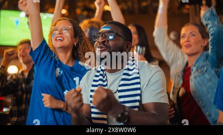 Die Mitglieder des Fußballclubs jubeln ihr Team an und spielen in einem Finale des Internationalen Pokals. Unterstützende Fans, die in einer Bar stehen, jubeln, die Hände heben und schreien. Freunde feiern den Sieg nach dem Tor. Stockfoto