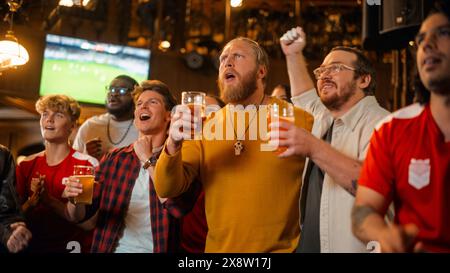 Gruppe von Freunden, die sich ein Live-Fußballspiel im Fernsehen in einer Sportbar ansehen. Drei Männer jubeln und schreien. Junge Menschen, die Biergläser feiern und anstoßen, wenn das Team die Fußball-Weltmeisterschaft gewinnt. Stockfoto