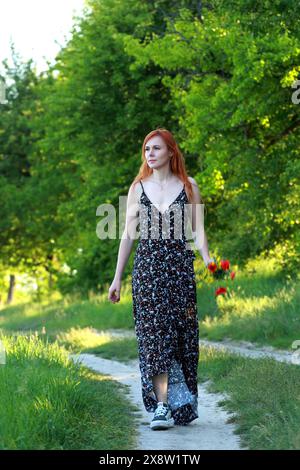 Ein Mädchen mit wilden Mohnblumen genießt die Aussicht von einem Hügel in der Nähe des Flusses. Freude, Glück, Gelassenheit. Wilde Mohnblumen am Fluss. Stockfoto