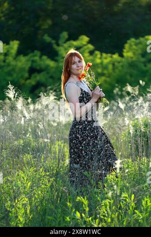 Ein Mädchen mit wilden Mohnblumen genießt die Aussicht von einem Hügel in der Nähe des Flusses. Freude, Glück, Gelassenheit. Wilde Mohnblumen am Fluss. Stockfoto