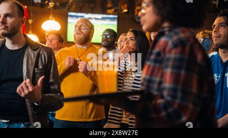 Die Mitglieder des Fußballclubs jubeln ihr Team an und spielen in einem Finale des Internationalen Pokals. Unterstützende Fans, die in einer Bar stehen, jubeln, die Hände heben und schreien. Freunde feiern den Sieg nach dem Tor. Stockfoto