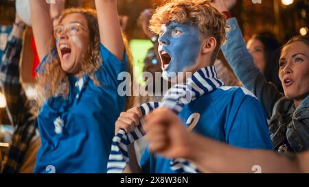 Eine Gruppe von Fußballfans mit farbigen Gesichtern, die ein Live-Fußballspiel in einer Sportbar anschauen. Leute jubeln ihr Team an. Der Spieler erzielt ein Tor und die Zuschauer feiern den Sieg der Meisterschaft. Stockfoto
