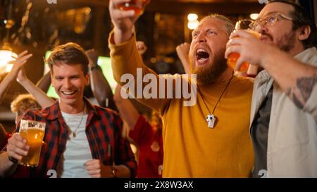 Gruppe von Fußballfans, die ein Live-Fußballspiel in einer Sportbar anschauen. Drei männliche Freunde stehen vor einem Fernseher, stoßen Biergläser an und feiern das Tor und den Meisterschaftsgewinn. Stockfoto