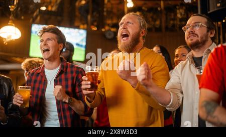 Gruppe von Freunden, die sich ein Live-Fußballspiel im Fernsehen in einer Sportbar ansehen. Drei Männer jubeln und schreien. Junge Menschen, die Biergläser feiern und anstoßen, wenn das Team die Fußball-Weltmeisterschaft gewinnt. Stockfoto