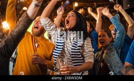 Die Mitglieder des Fußballclubs jubeln ihr Team an und spielen in einem Finale des Internationalen Pokals. Unterstützende Fans, die in einer Bar stehen, jubeln, die Hände heben und schreien. Freunde feiern den Sieg nach dem Tor. Stockfoto