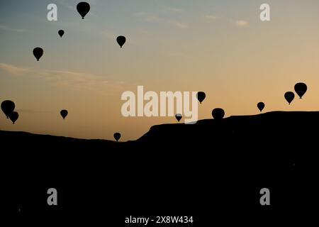 Heißluftballons bilden eine Silhouette vor dem Morgenhimmel in Kappadokien und schaffen eine ruhige und fesselnde Szene. Die Ballons schweben anmutig über die rugge Stockfoto