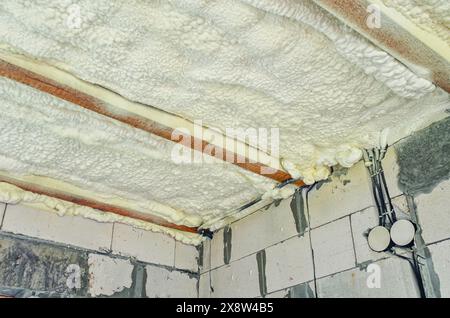 Isolierung der Decke im Haus mit Polyurethanschaum. Dämmschaum zwischen Holzbalken Stockfoto