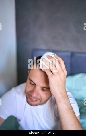 Der Mann massiert seinen Kopf mit einem elektrischen Massagegerät für Haarwuchs Stockfoto