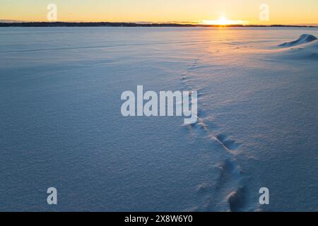 Blick auf die Fußstapfen auf einem gefrorenen und verschneiten See in Finnland bei Sonnenuntergang. Wunderschöne natürliche und ruhige Winterlandschaft. Kopierbereich. Stockfoto