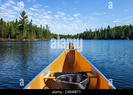 Gelbes Kanu mit Fischernetz auf einem blauen See mit Kiefern entlang der Küste an einem sonnigen Sommernachmittag im Norden von Minnesota Stockfoto