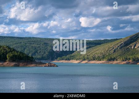 Das Bild zeigt einen ruhigen See, der von grünen Hügeln und bewaldeten Bergen umgeben ist. Stockfoto