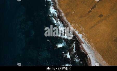 Sonniger Herbsttag am Ufer mit sanften Meereswellen. Clip. Blick aus der Vogelperspektive auf die Hügel, die von verwelktem Gras und dunkelblauem Meer bedeckt sind. Stockfoto