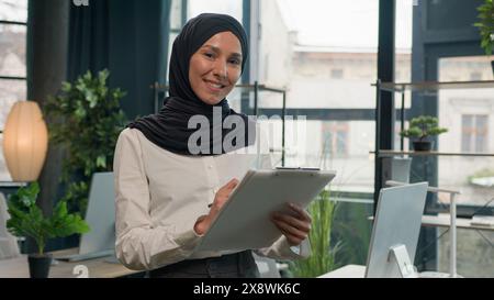 Glückliche muslimische Islamfrau Arabisches Mädchen im Hijab Personalmanager Sekretärin mit Papiertablett Schreiben Sie Notizen signieren Daten in Notizen Tablet Schreiben To-Do-Liste Geschäft Stockfoto