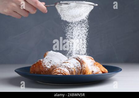 Frau mit einem Sieb, das Puderzucker auf Croissants streut, am weißen Holztisch, Nahaufnahme Stockfoto