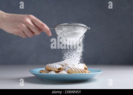 Frau mit einem Sieb, das Puderzucker auf Kekse streut, an weißem Holztisch, Nahaufnahme Stockfoto